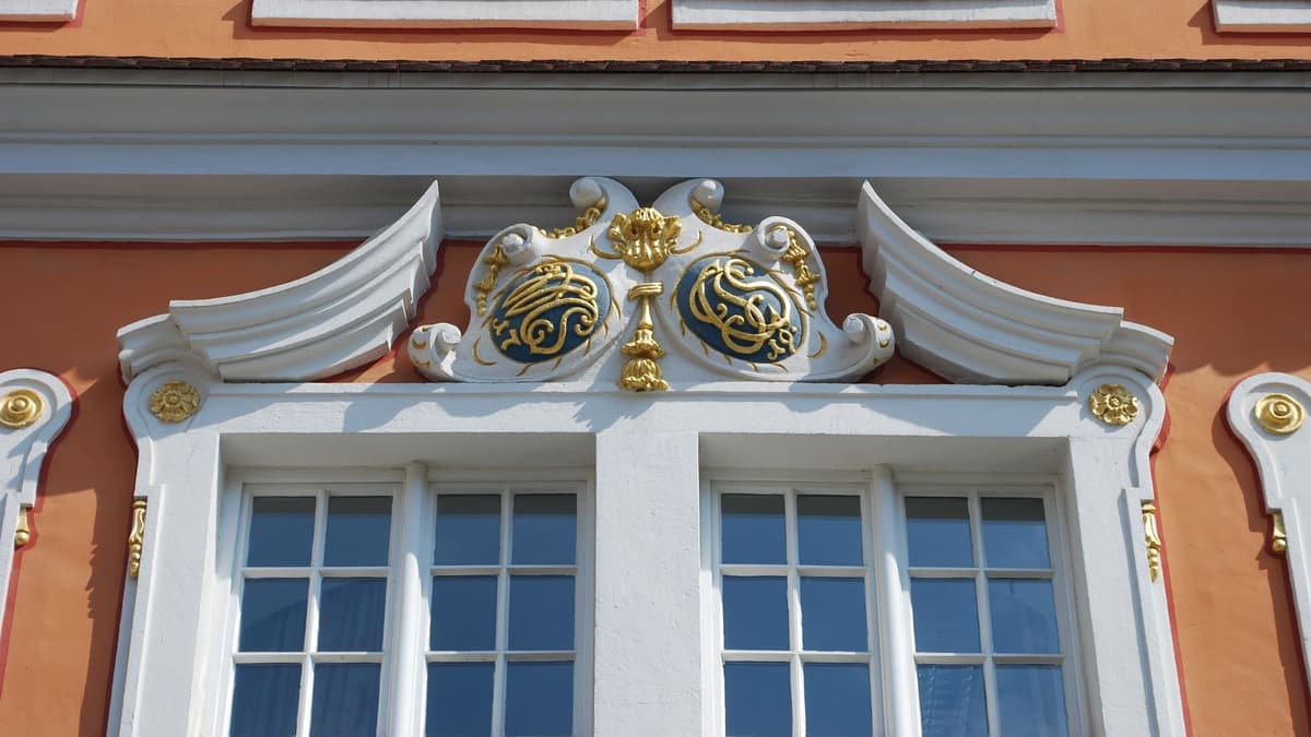 Fensterbekrönung mit geschweiftem Sprenggiebel und Doppelkartusche mit Mogrammen und Baujahr
