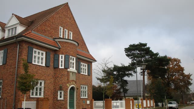 Postgebäude mit Nebengebäuden, straßenseitiger Grundstückseinfriedung und Hofpflaster